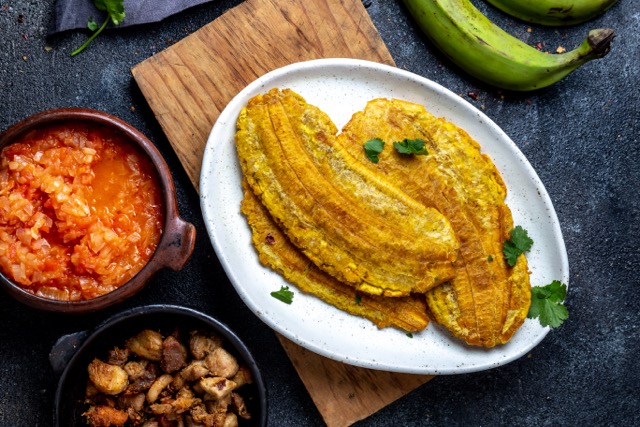 COLOMBIAN CARIBBEAN CENTRAL AMERICAN FOOD. Patacon or toston, fried and flattened whole green plantain banana on white plate. Black background, top view